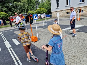 Zdjęcie przedstawia: dzieci na hulajnogach na miasteczku rowerowym. w tle umundurowani policjanci