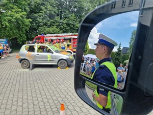 Zdjęcie przedstawia: w lusterku umundurowanego policjanta. Z tyłu widać akcję strażaków