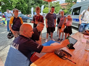 Zdjęcie przedstawia: dwóch mężczyzn (jeden umundurowany policjant) uczący dzieci jak udzielić pierwszej pomocy