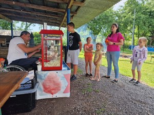 Zdjęcie przedstawia: mężczyznę który podaje popcorn osobom stojącym w kolejce.