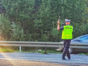 Zdjęcie przedstawia: policjanta ruchu drogowego, który za pomocą tarczy wydaje kierowcy polecenie do zatrzymania.