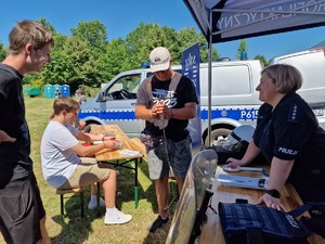 Zdjęcie przedstawia: młodych ludzi podczas rozmowy z policjantką i oglądania kajdanek na ręce i nogi.