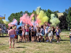 Zdjęcie przedstawia: grupę ludzi obsypującą się kolorowymi proszkami.