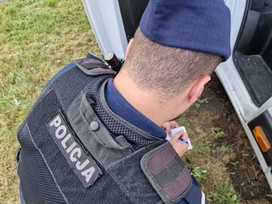 Zdjęcie przedstawia: umundurowany policjant robiący zapiski w notatniku.