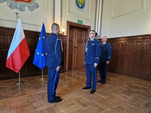 Zdjęcie przedstawia: trzech policjantów. Scena składania meldunku.