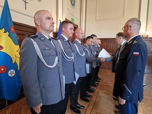 Zdjęcie przedstawia: rząd policjantów naprzeciwko których stoją ich przełożeni i wręczają nominacje na wyższy stopień policyjny oraz składają gratulacje.