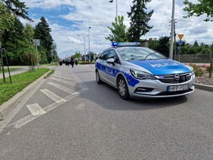 Zdjęcie przedstawia: oznakowany radiowóz a za nim maszerujących ludzi.