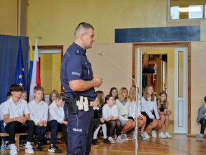 Zdjęcie przedstawia: policjanta mówiącego do mikrofonu.