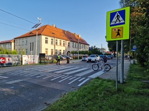 Zdjęcie przedstawia: dziewczynkę, która przechodzi przez przejście dla pieszych pchając rower.