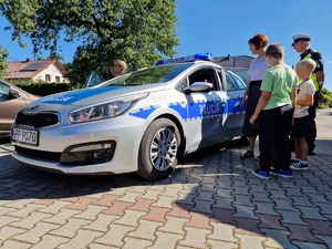 Zdjęcie przedstawia: grupę dzieci przy policyjnym radiowozie. Obok umundurowany policjant.