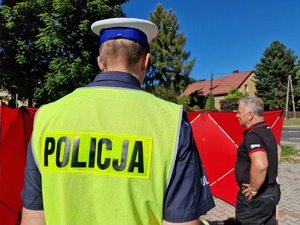 Zdjęcie przedstawia: policjanta w kamizelce odblaskowej, z tyłu mężczyzna.