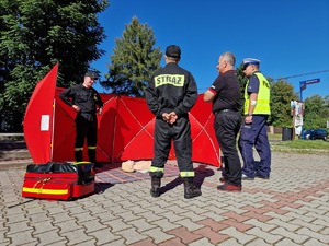 Zdjęcie przedstawia: policjanta i strażaków podczas rozmowy z mężczyzną.