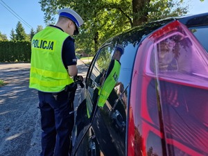 Zdjęcie przedstawia: policjanta gdy stoi obok samochodu i rozmawia z kierowcą.