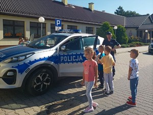 Zdjęcie przedstawia grupę dzieci oglądających policyjny radiowóz, obok policjant.