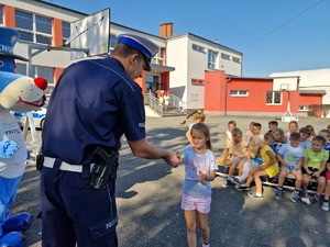 Zdjęcie przedstawia: mundurowego który daje dziecku zawieszkę odblaskową.