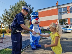 Zdjęcie przedstawia: policjanta, który daje dziecku odblask, z tyłu policyjna maskotka.