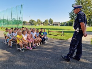 Zdjęcie przedstawia: policjanta, który stoi przed grupą słuchających go dzieci.