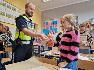 Zdjęcie przedstawia: policjanta, która daje dziecku zawieszkę odblaskową.