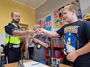 Zdjęcie przedstawia: policjanta, która daje dziecku zawieszkę odblaskową.