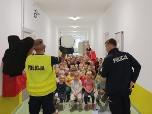 Zdjęcie przedstawia: dwóch umundurowanych policjantów podczas pogadanki przed grupą przedszkolaków.