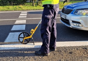 Zdjęcie przedstawia: policjanta podczas pomiaru na miejscu wypadku.