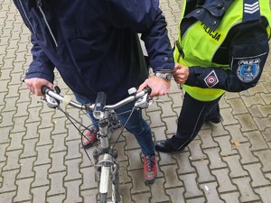 Zdjęcie przedstawia: policjanta, który zapina kajdanki na ręce mężczyźnie, który stoi okrakiem nad rowerem.