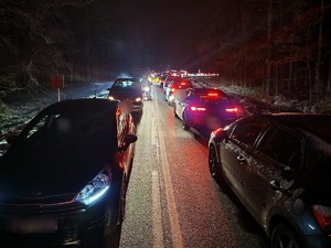 Zdjęcie przedstawia: jednię po jednym pasie w każdym kierunku. Na drodze stoi sznur samochodów w obu kierunkach.