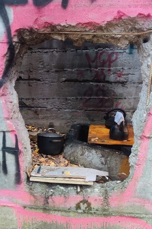 Zdjęcie przedstawia: dziurę w murze przez którą widać garnki i naczynia.