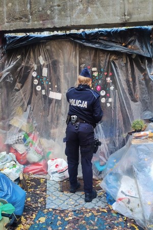 Zdjęcie przedstawia: policjantkę przed miejscem przebywania osób bezdomnych.