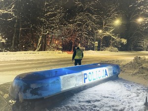 Zdjęcie przedstawia: oznakowany radiowóz policyjny przy jezdni i umundurowanego policjanta na drodze.