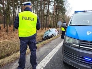 Zdjęcie przedstawia: umundurowanego policjanta, radiowóz i samochód w rowie.