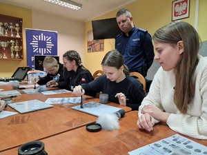 Zdjęcie przedstawia: kadetów podczas warsztatów, za nimi stoi policjant.