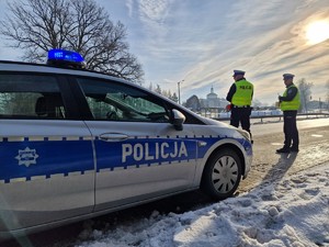 Zdjęcie przedstawia: policyjny radiowóz, obok stoją policjanci.