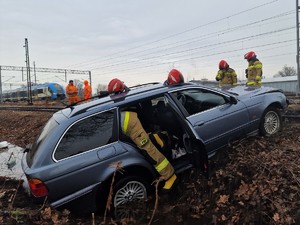 Zdjęcie przedstawia: pojazd uszkodzony po zdarzeniu drogowym, z tyłu widoczny pociąg.