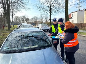 Zdjęcie przedstawia: dwoje umundurowanych policjantów wraz z kobietą w kamizelce odblaskowej podczas rozmowy z kierującym.