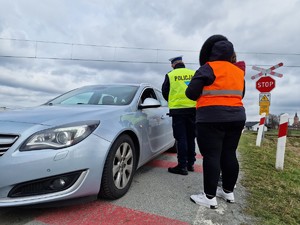 Zdjęcie przedstawia: mundurowego i przedstawicieli Kolei Śląskich podczas działań profilaktycznych na przejeździe kolejowym.