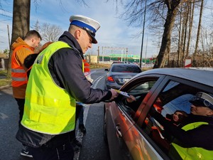 Zdjęcie przedstawia: policjanta wręczającego materiały edukacyjne uczestnikom ruchu.