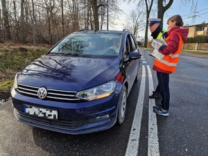 Zdjęcie przedstawia: policjanta wraz z kobietą w kamizelce odblaskowej podczas działań edukacyjnych na przejeździe kolejowym.