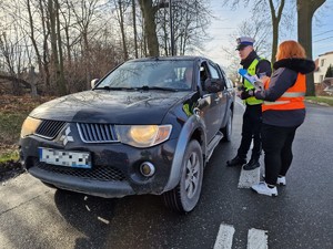 Zdjęcie przedstawia: policjanta wraz z kobietą podczas rozmowy z kierowcą samochodu osobowego.