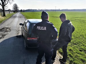 Zdjęcie przedstawia umundurowanego policjanta i mężczyznę. Osoby stoją obok samochodu osobowego.