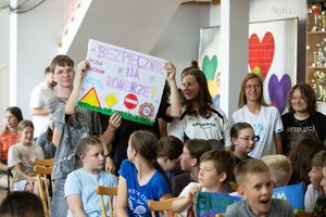 Na zdjęciu młode osoby z plakatem, na którym widnieje napis o treści: Bezpiecznie na rowerze