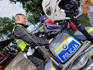 Zdjęcie przedstawia: policjanta który coś objaśnia dziecku które siedzi na motocyklu.