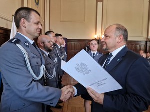 Zdjęcie przedstawia: policjanta, któremu gratulacje składa mężczyzna w garniturze.