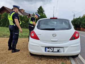 Zdjęcie przedstawia: dwóch policjantów podczas kontroli drogowej stoi przy samochodzie.