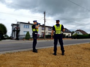 Zdjęcie przedstawia: dwóch policjantów, którzy stoją przy drodze.