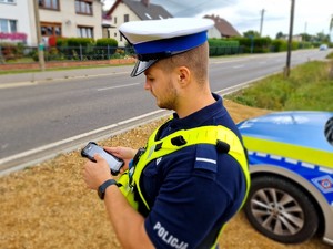 Zdjęcie przedstawia: policjanta z urządzeniem sprawdzającym w dłoniach.