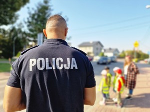 Zdjęcie przedstawia: policjant przy przejściu dla pieszych z dziećmi.