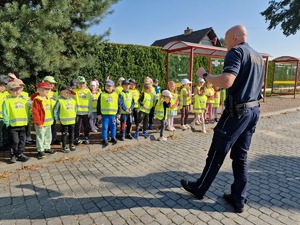 Zdjęcie przedstawia: umundurowanego policjanta stojącego przed grupą dzieci