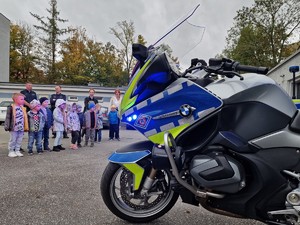 Zdjęcie przedstawia: 
Dzieci stojące przy motocyklach policyjnych oraz dwóch funkcjonariuszy i opiekunki przedszkolaków.