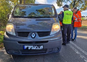 Zdjęcie przedstawia: 
Przód dużego samochodu oraz funkcjonariusza policji rozmawiającego z kierowcą i dwojgiem przedstawicieli Kolei Śląskich.